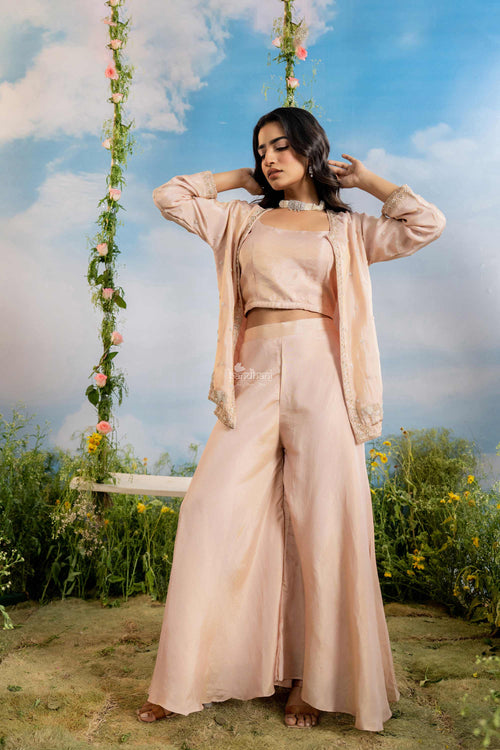 Woman in a peach outfit standing on a grassy area with a floral swing and blue sky in the background