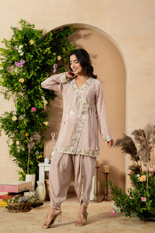 Woman in a light pink traditional outfit standing in a decorated room with plants and flowers.
