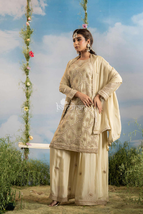 Woman in traditional beige outfit standing outdoors with a decorative swing and floral decorations.