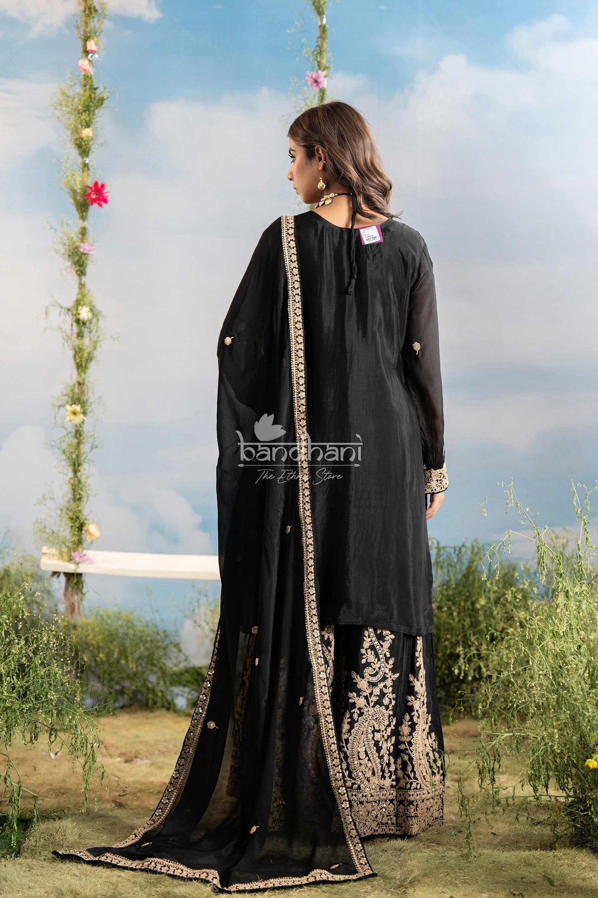 Woman wearing a black traditional outfit with floral decorations against a natural background