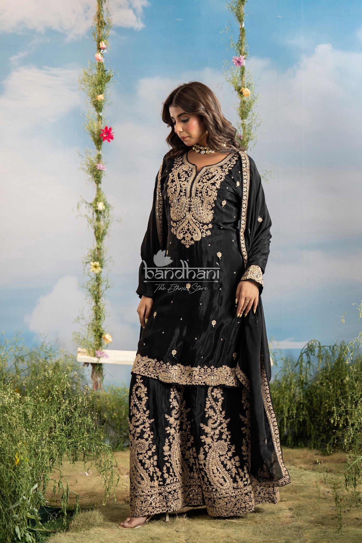 Woman wearing a black and gold traditional outfit with 'bandhani' branding against a natural background.