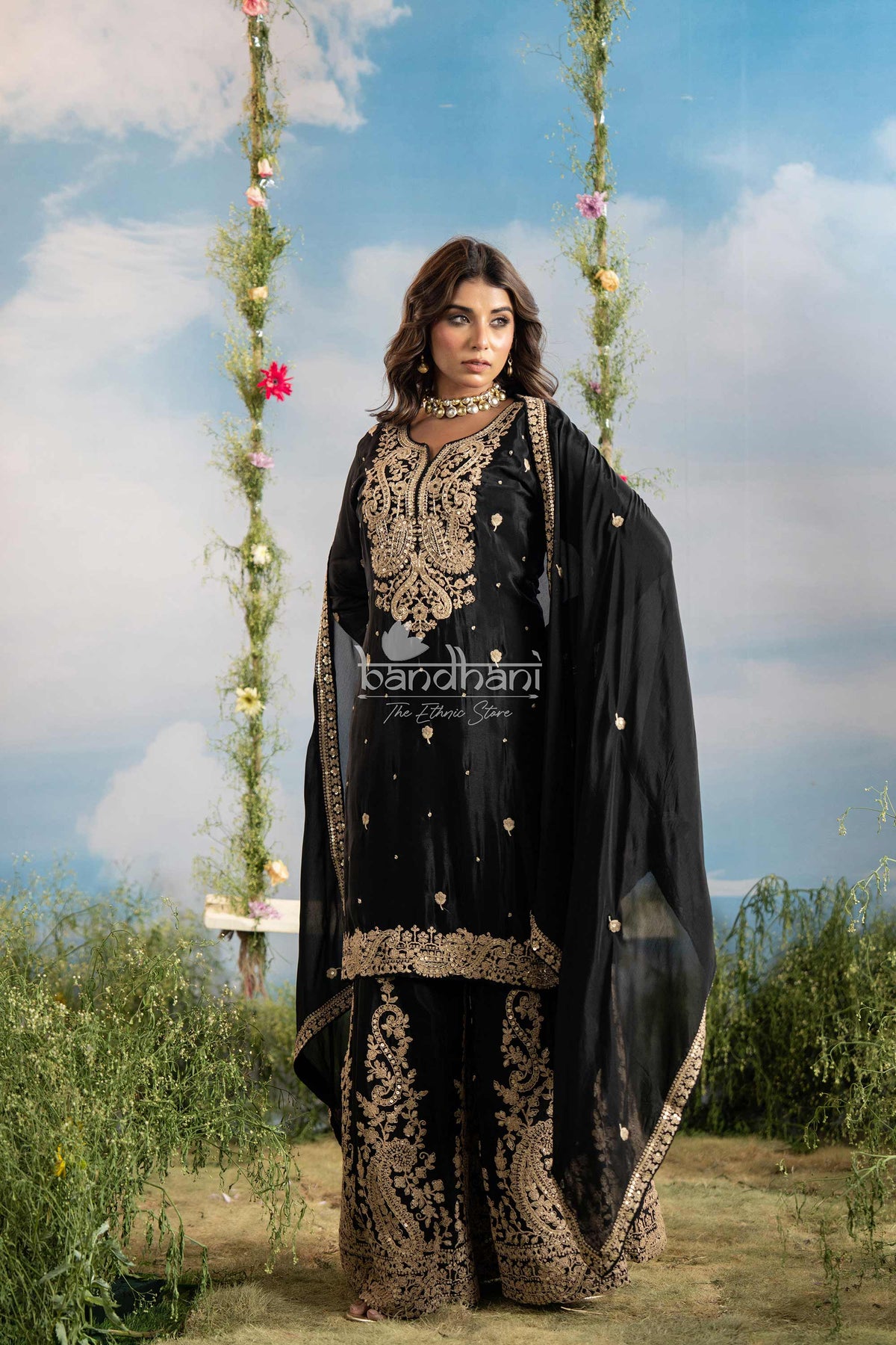 Woman in black embroidered traditional outfit with 'bandhani' branding against a scenic background.