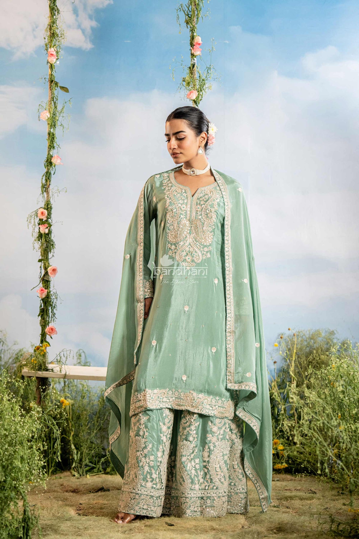 Woman in a traditional green outfit with floral decorations against a blue sky.