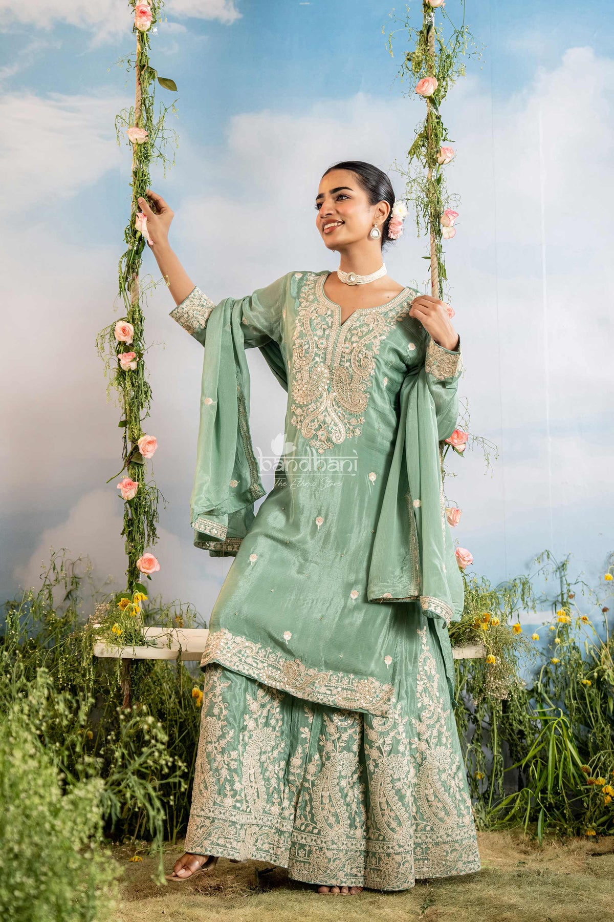 Woman in traditional green outfit on a swing with floral decorations against a blue sky.