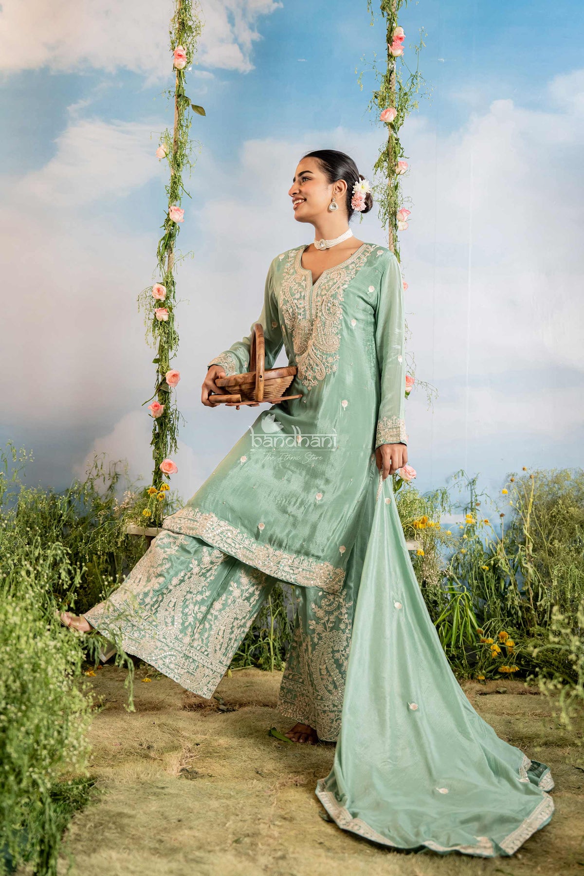 Woman in a light green traditional outfit sitting on a floral swing with a scenic background.