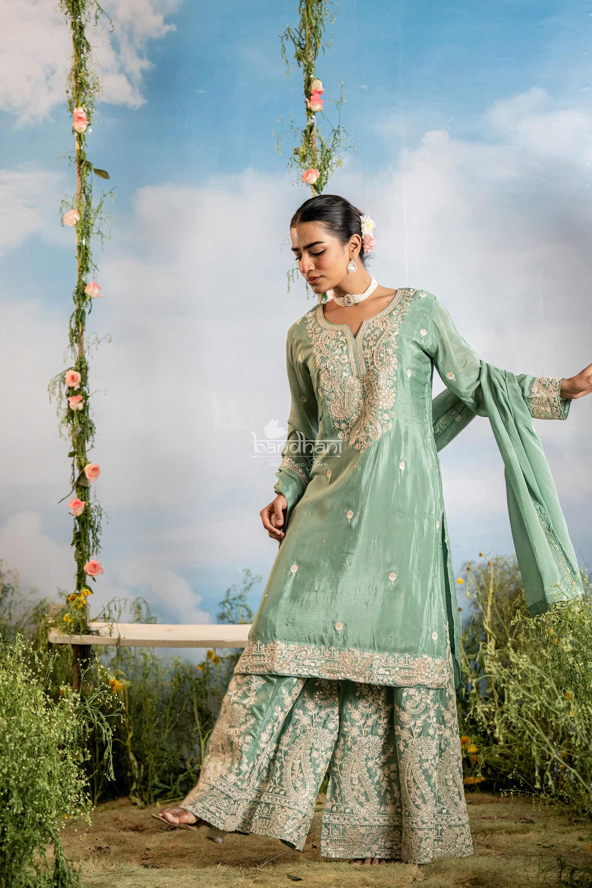Woman in a green traditional outfit standing outdoors with a floral swing in the background