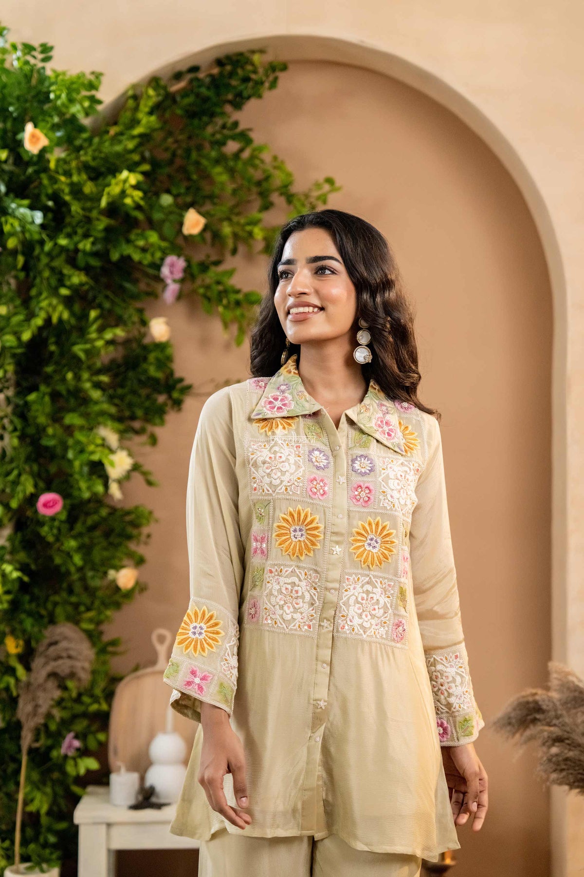 Woman wearing a beige embroidered co-ord set with floral patterns in an outdoor setting.