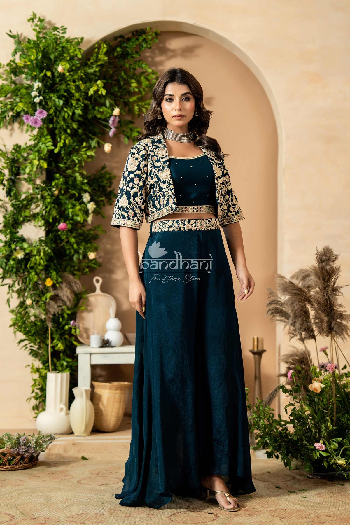 Woman in a dark blue outfit with a floral jacket standing in a decorated indoor setting.