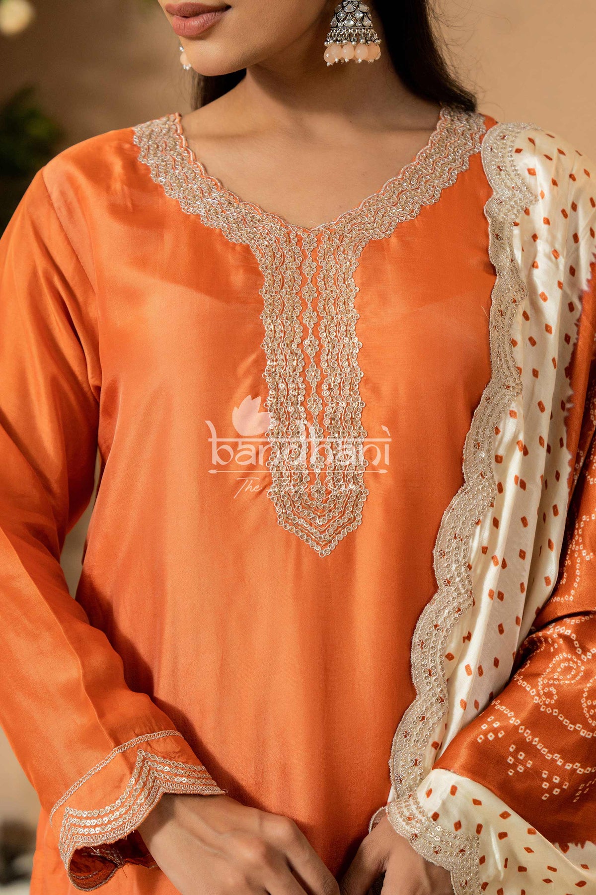 Orange traditional outfit with intricate white embroidery and bandhani design, featuring the brand 'bandhani'.