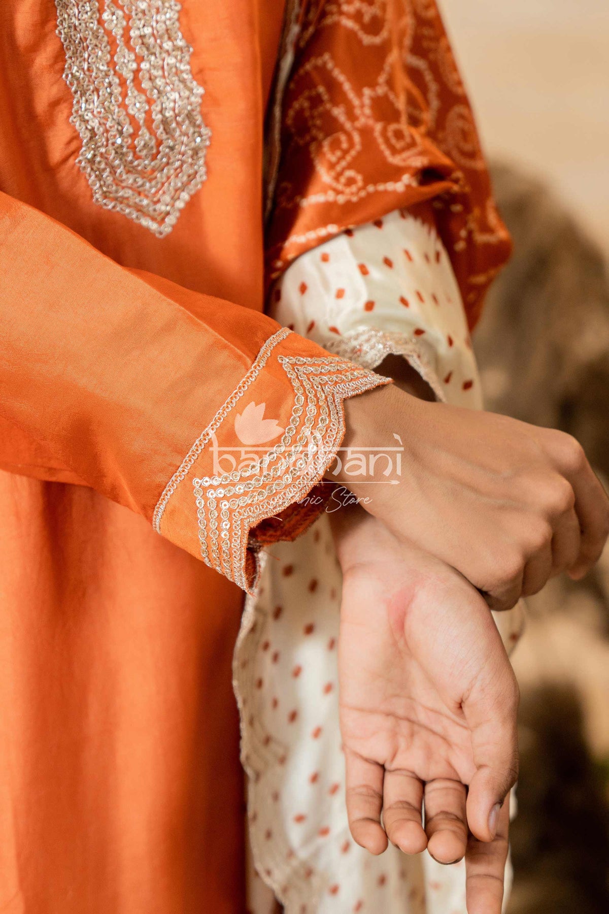 Close-up of an orange traditional outfit with intricate patterns, held by a person.
