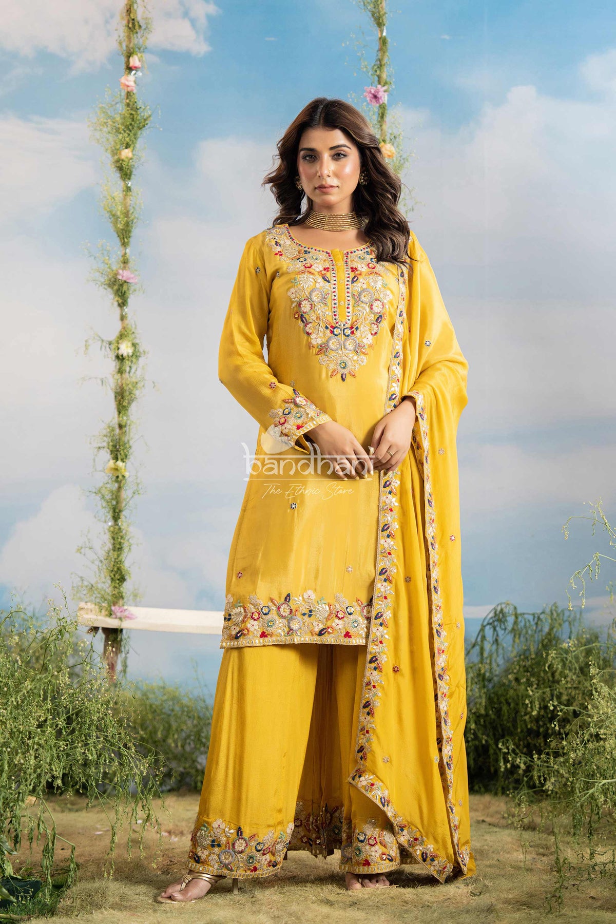 Woman in a yellow traditional outfit with floral embroidery standing outdoors.