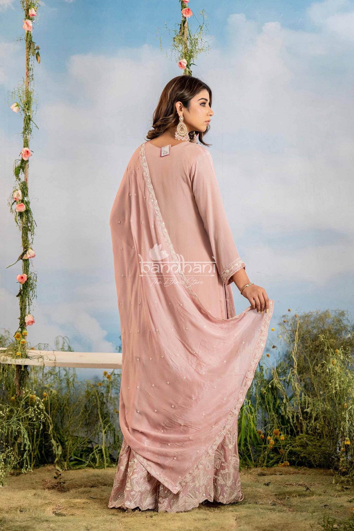 Woman in a pink saree standing outdoors with a decorated swing in the background