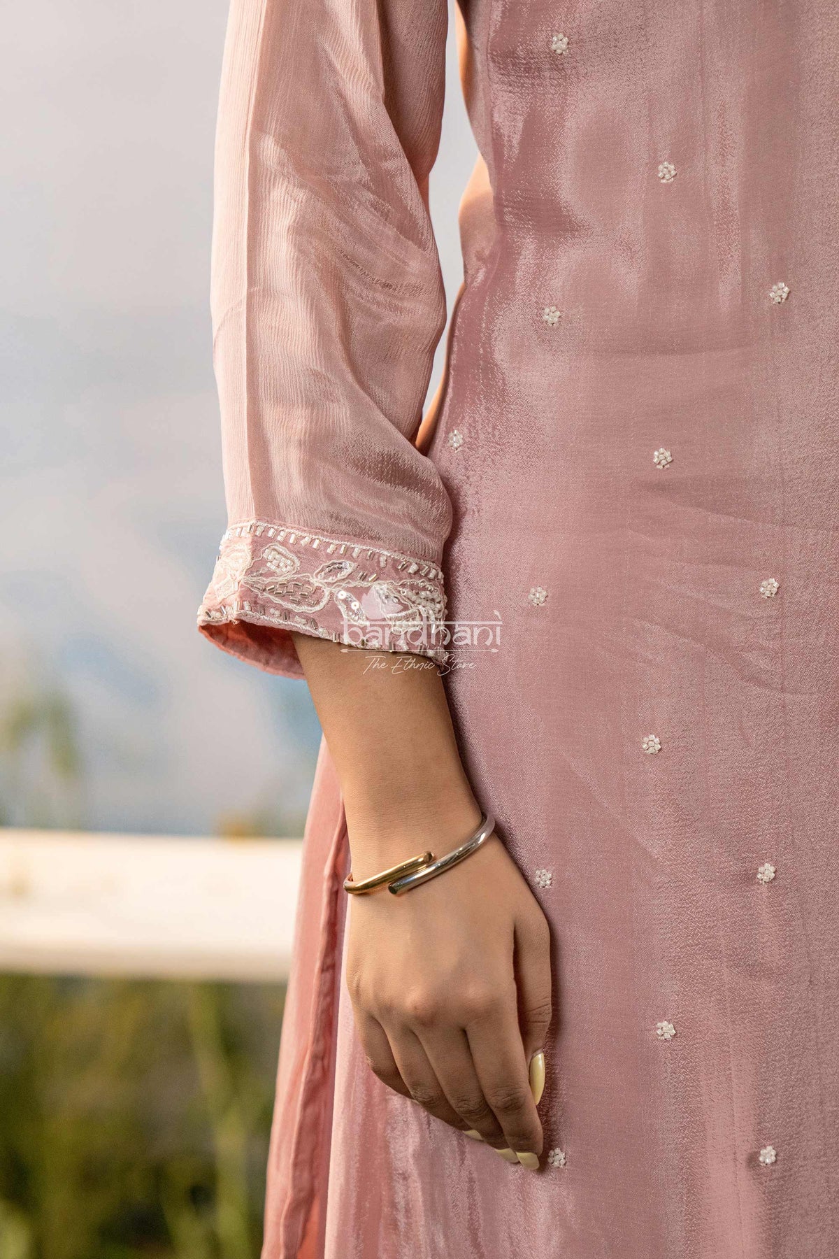 Close-up of a person wearing a pink traditional outfit with intricate designs, blurred natural background.