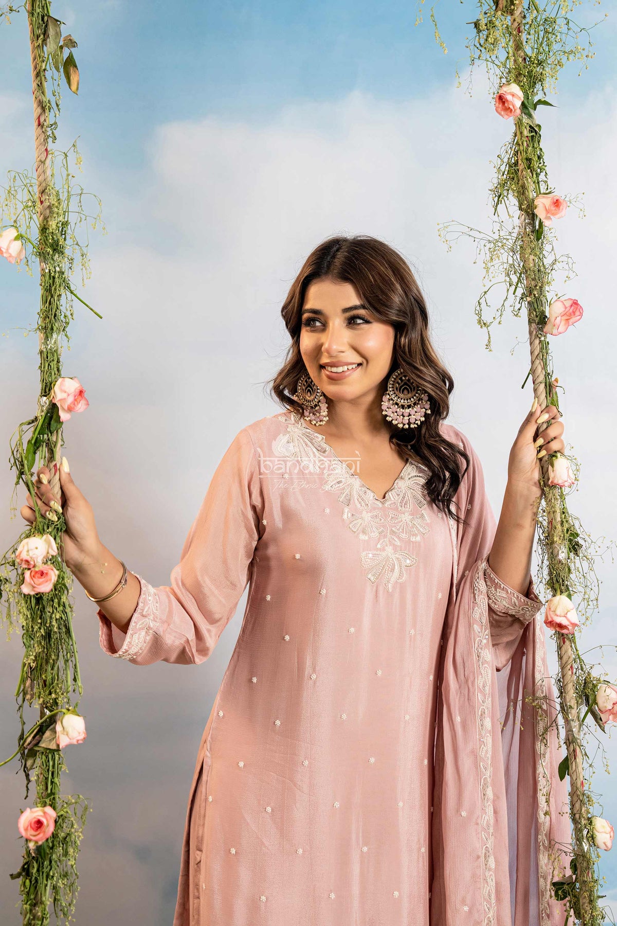 Woman in a pink traditional outfit with floral decorations against a blue sky.