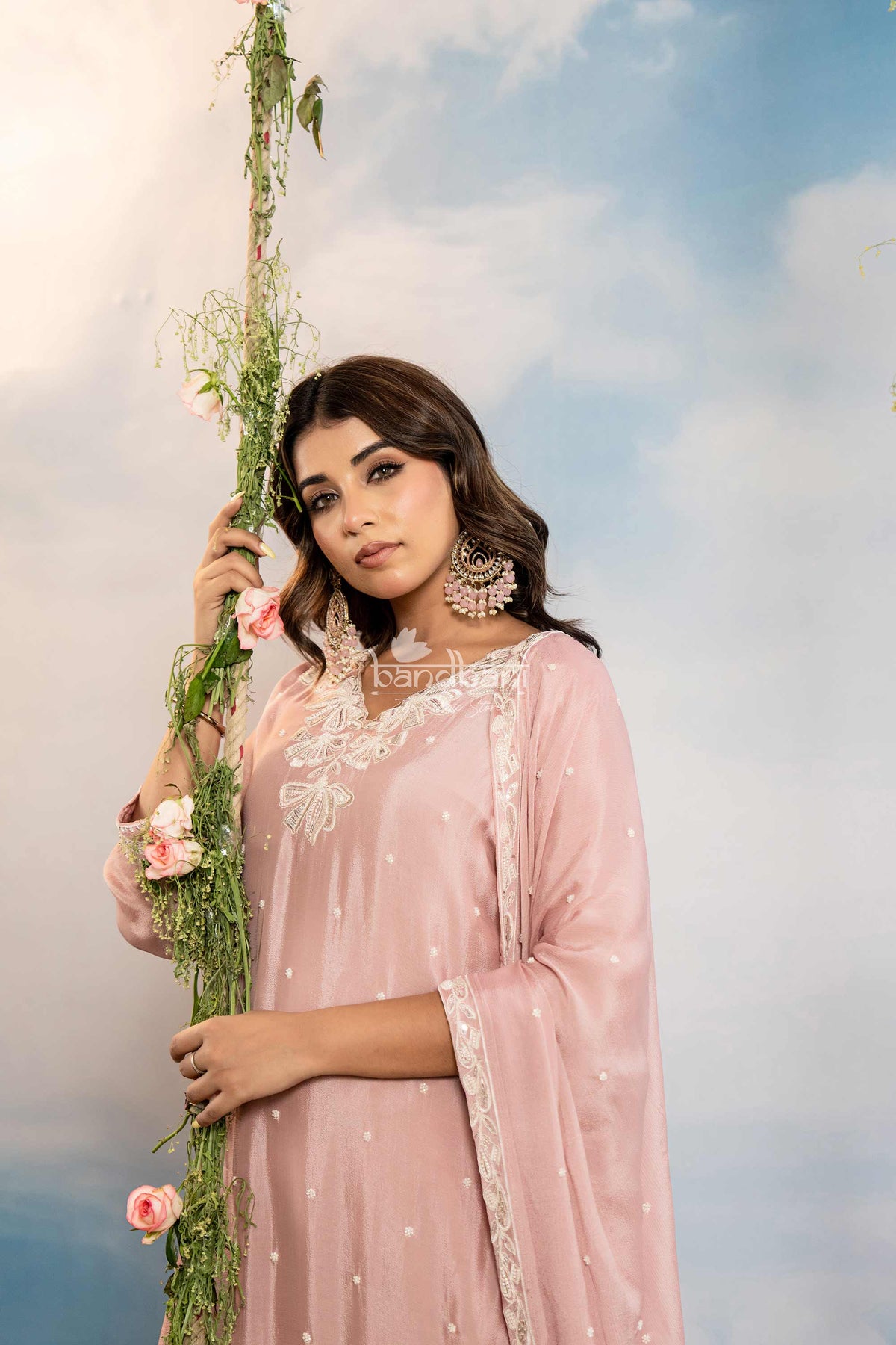 Woman in a pink traditional outfit holding flowers against a cloudy sky.