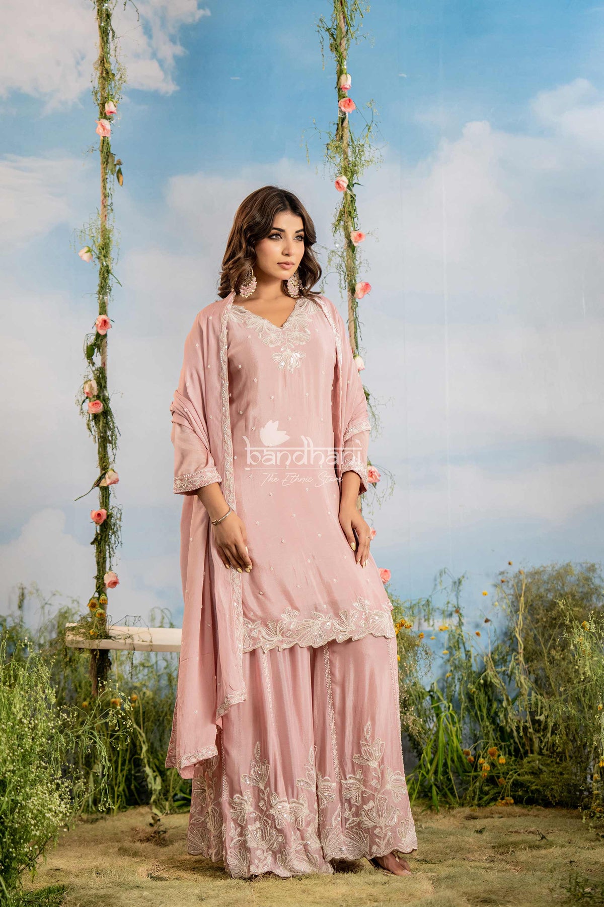 Woman in a pink traditional outfit standing on a grassy area with a scenic background