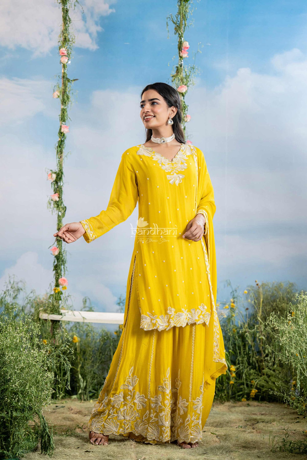 Woman in a yellow traditional outfit with floral decorations against a blue sky and greenery.