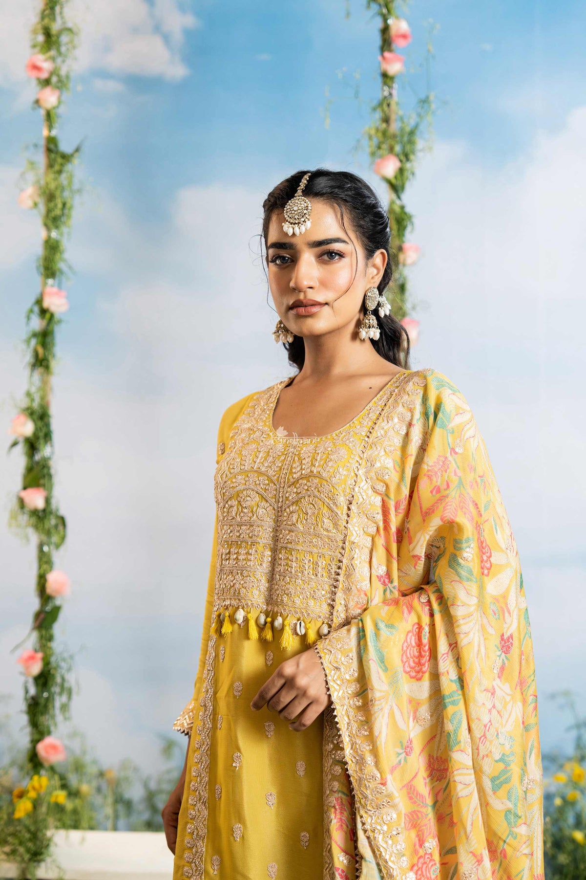 Woman in a yellow traditional outfit with floral decorations against a blue sky.