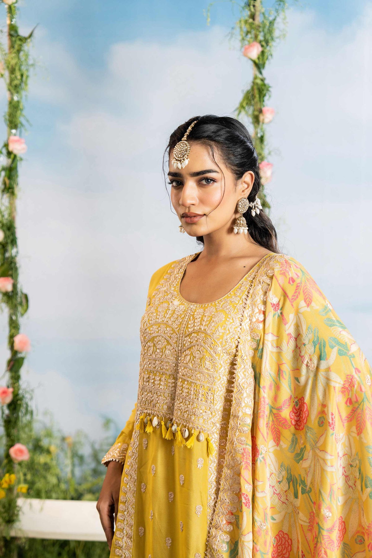 Woman in a yellow traditional outfit with floral patterns against a blurred natural background