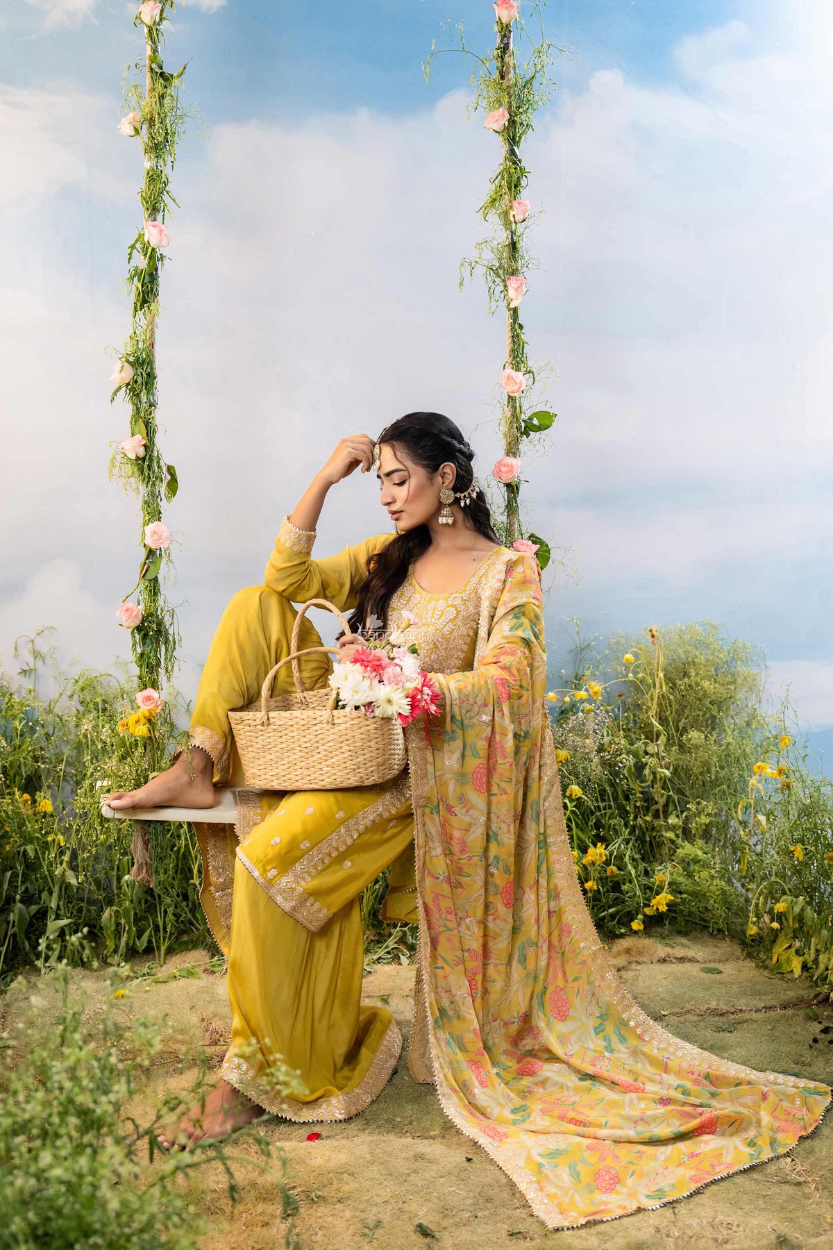Woman in a yellow saree sitting on a swing with flowers in a natural setting