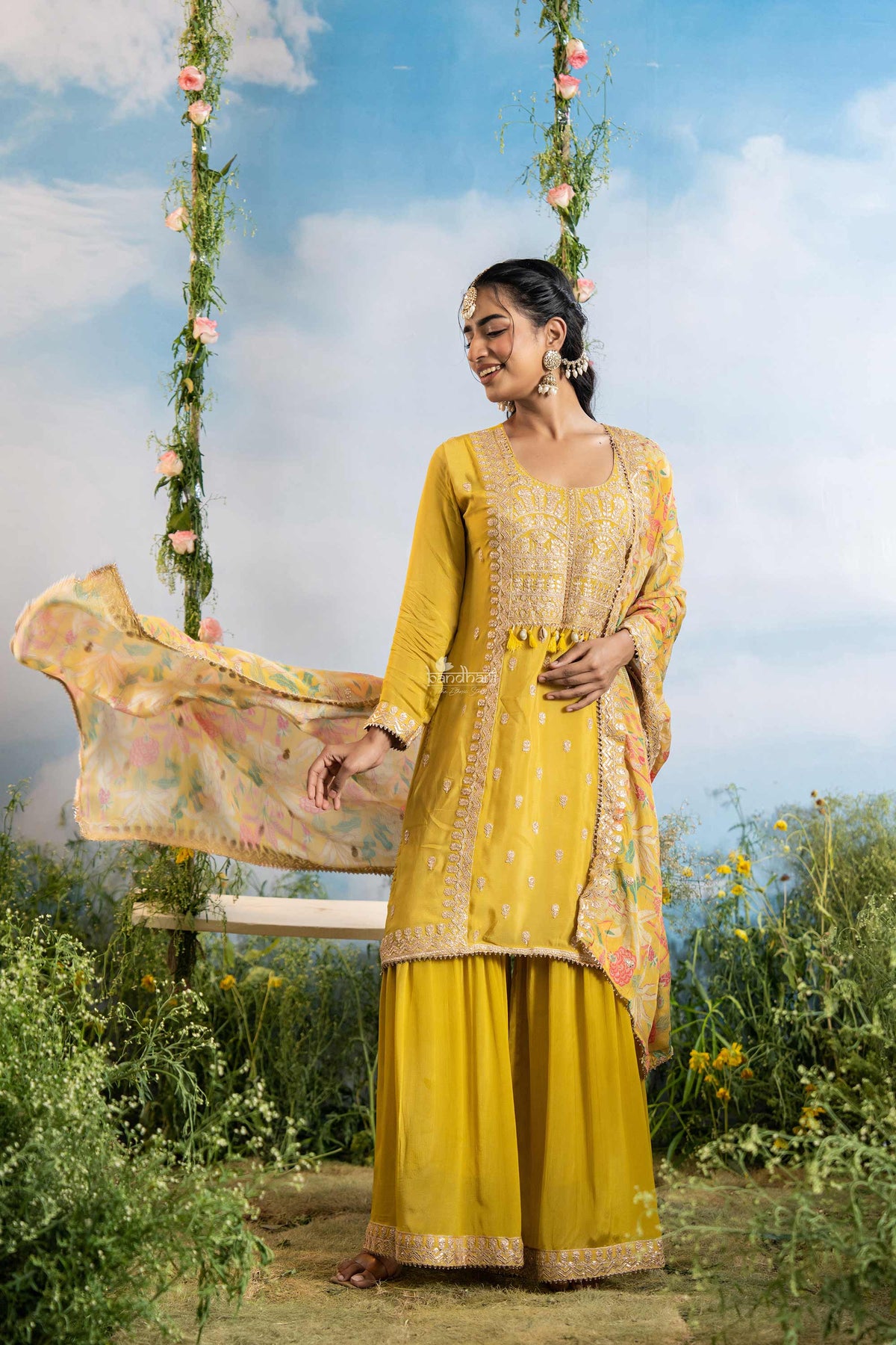 Woman in a yellow traditional outfit sitting on a swing with floral decorations against a blue sky.