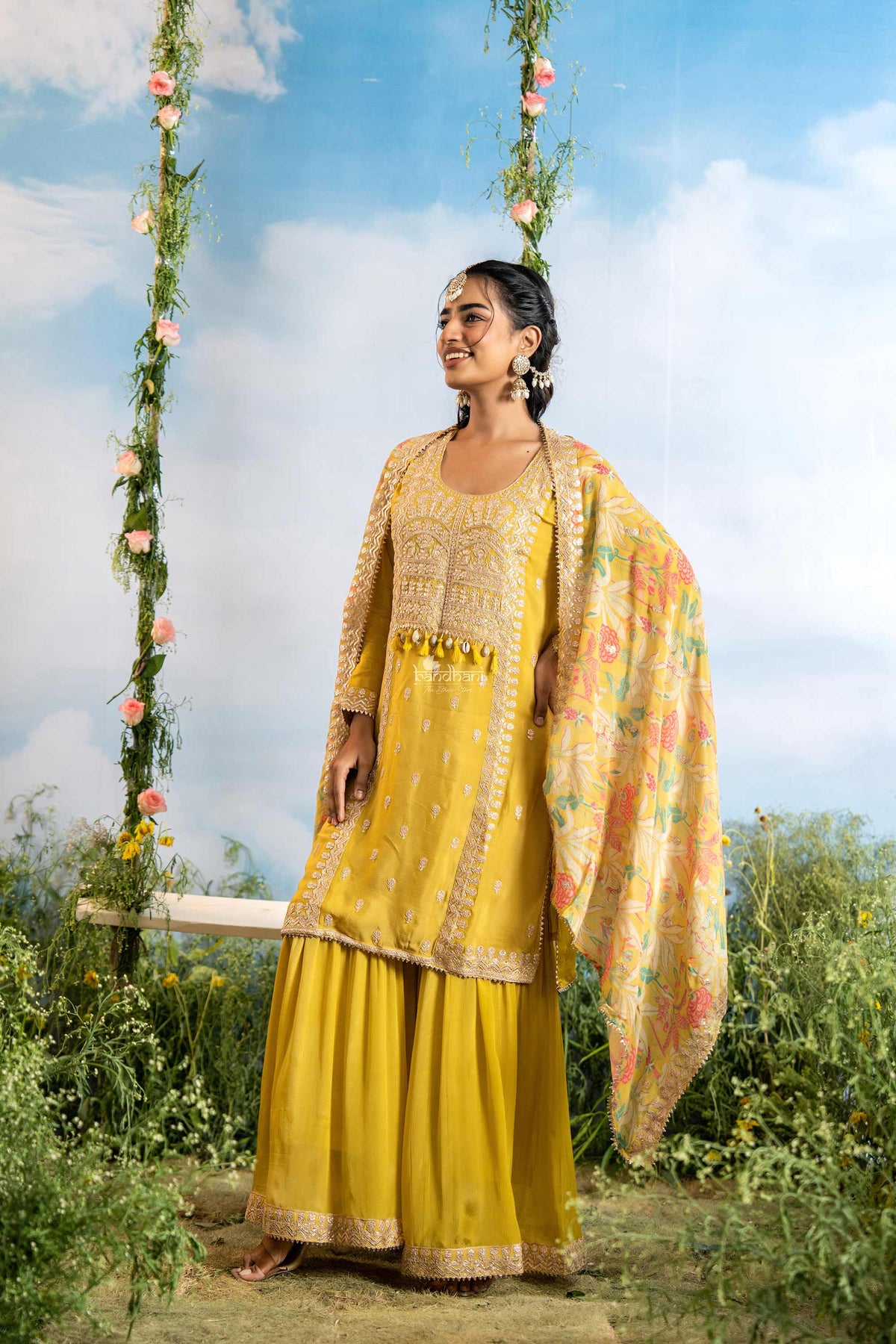 Woman in a yellow traditional outfit standing outdoors with floral decorations.