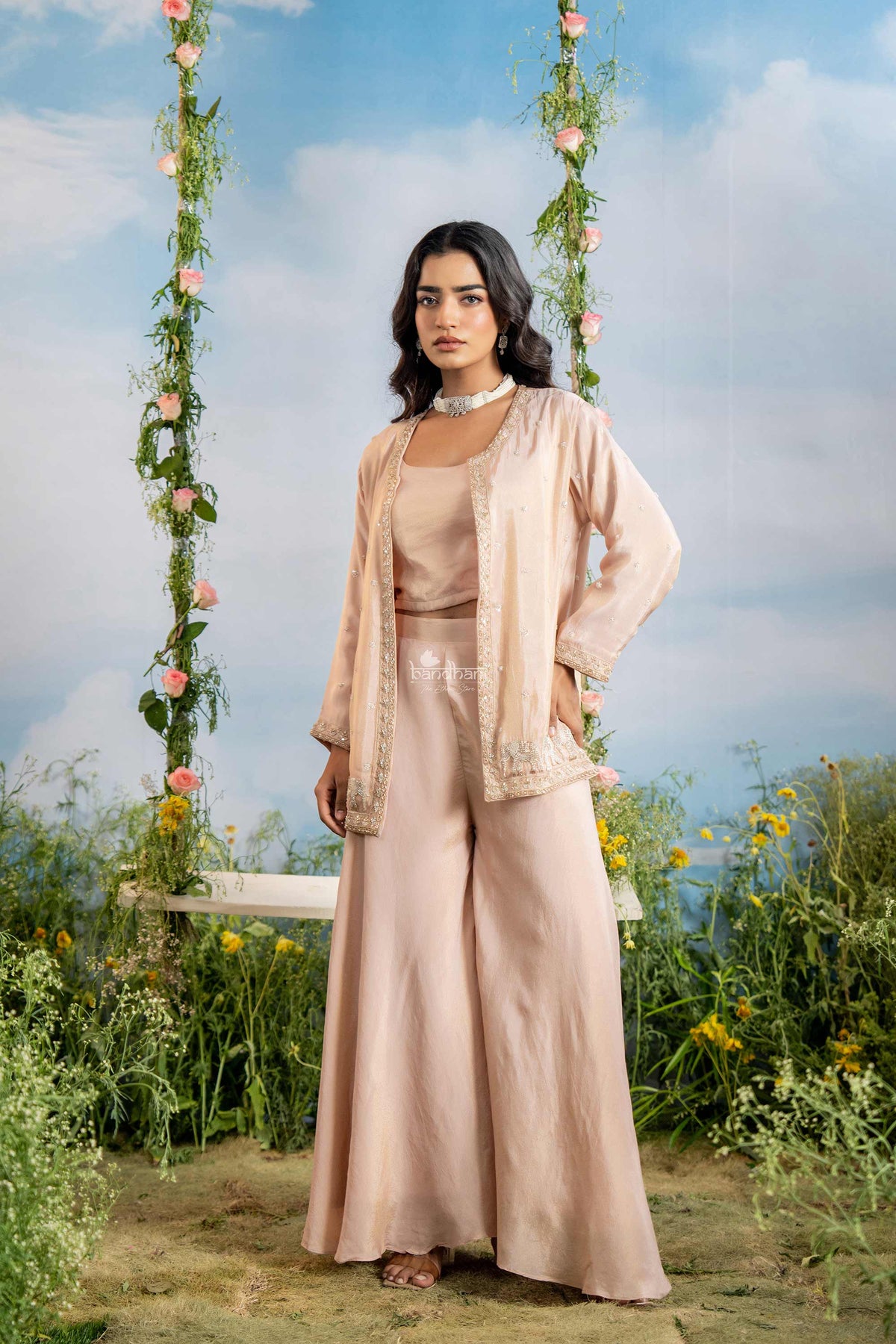 Woman in a beige outfit standing in a garden with floral decorations.