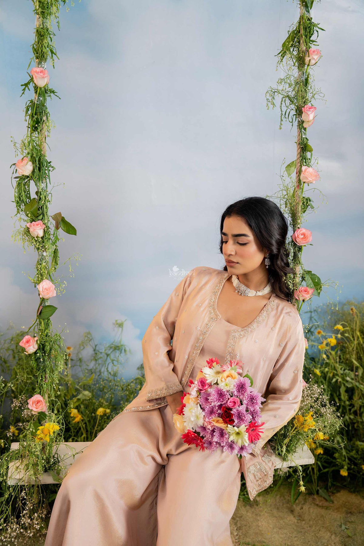 Woman in a beige outfit sitting on a floral swing with a blurred natural background