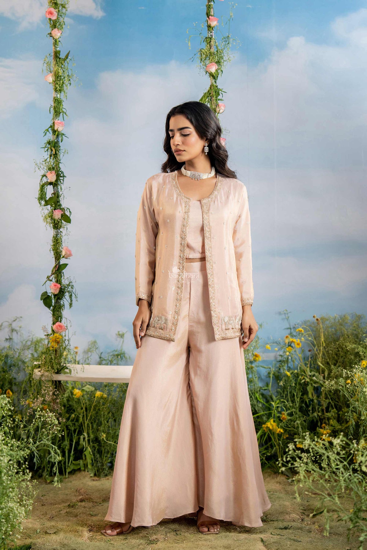 Woman in a beige traditional outfit standing in a garden with floral decorations.