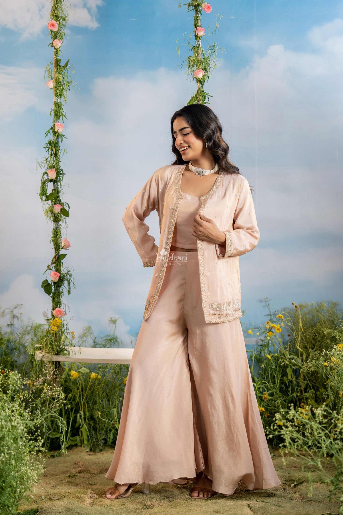 Woman in a beige traditional outfit standing under floral decorations with a scenic background