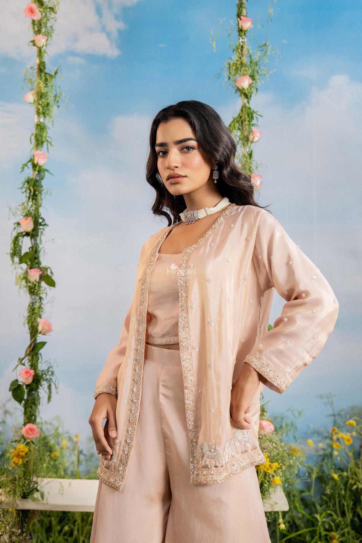 Woman in a beige outfit standing outdoors with floral decorations and a blue sky.
