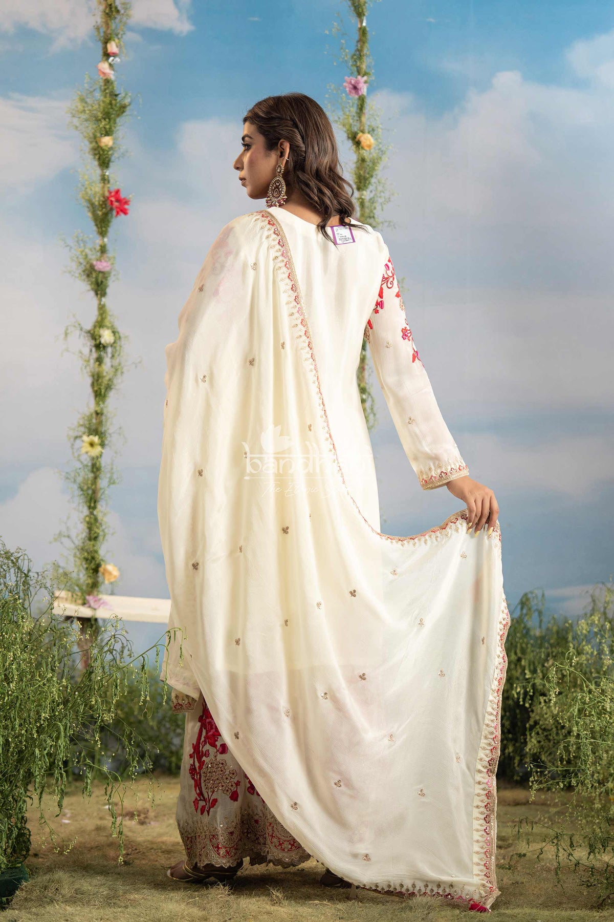 Woman in a white traditional outfit with red patterns standing outdoors against a blue sky.