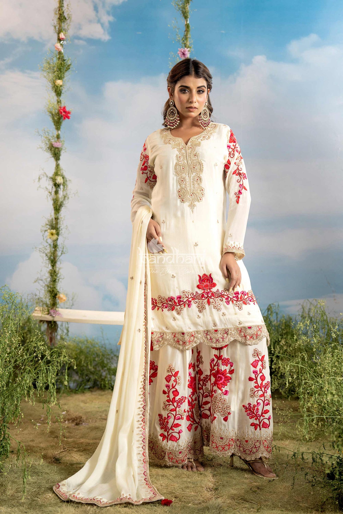 Woman in a white and red embroidered traditional outfit standing outdoors with a scenic background.