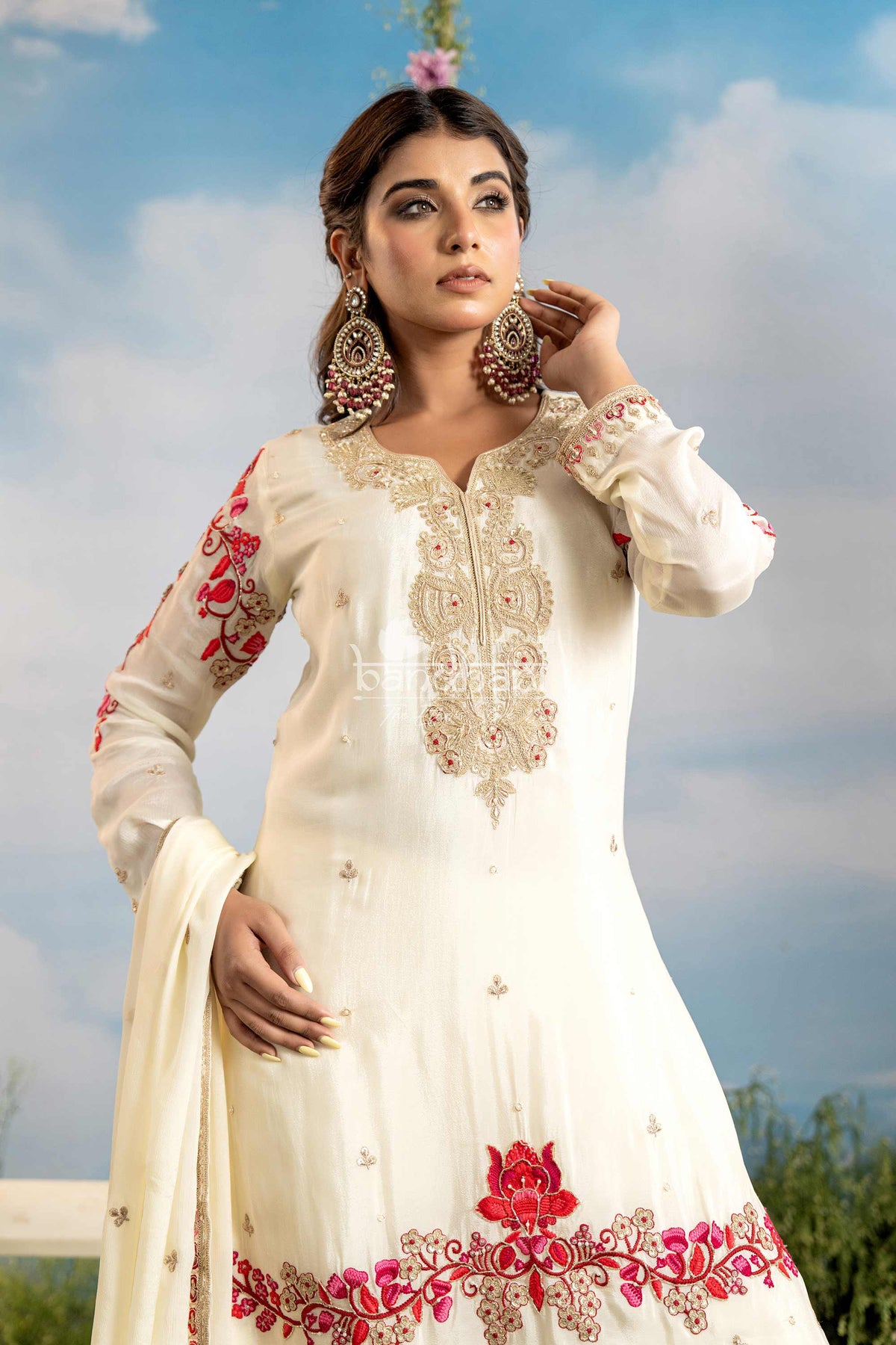 Woman wearing a white embroidered outfit with red details against a blue sky.
