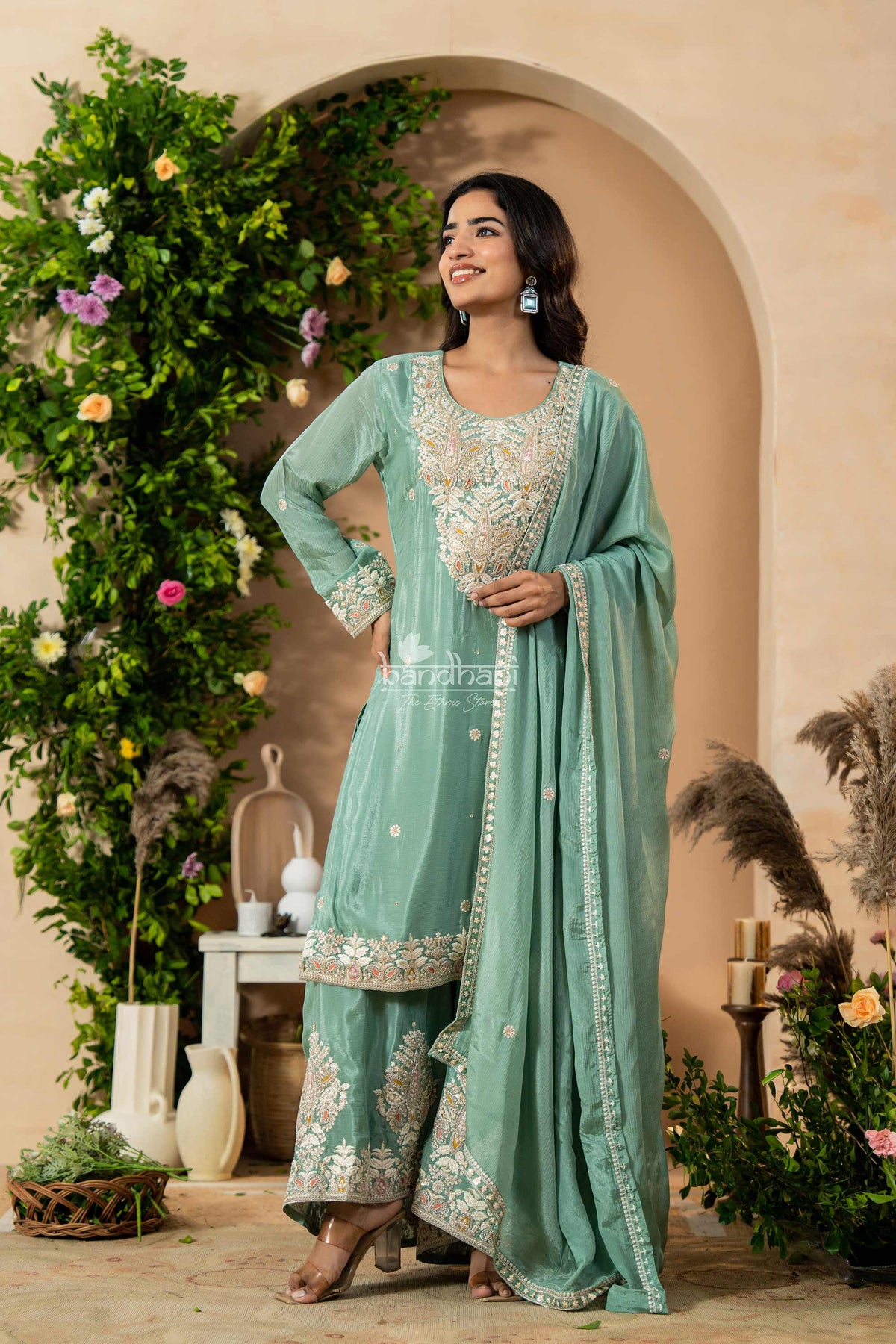 Woman in a light green traditional outfit with floral decorations in the background