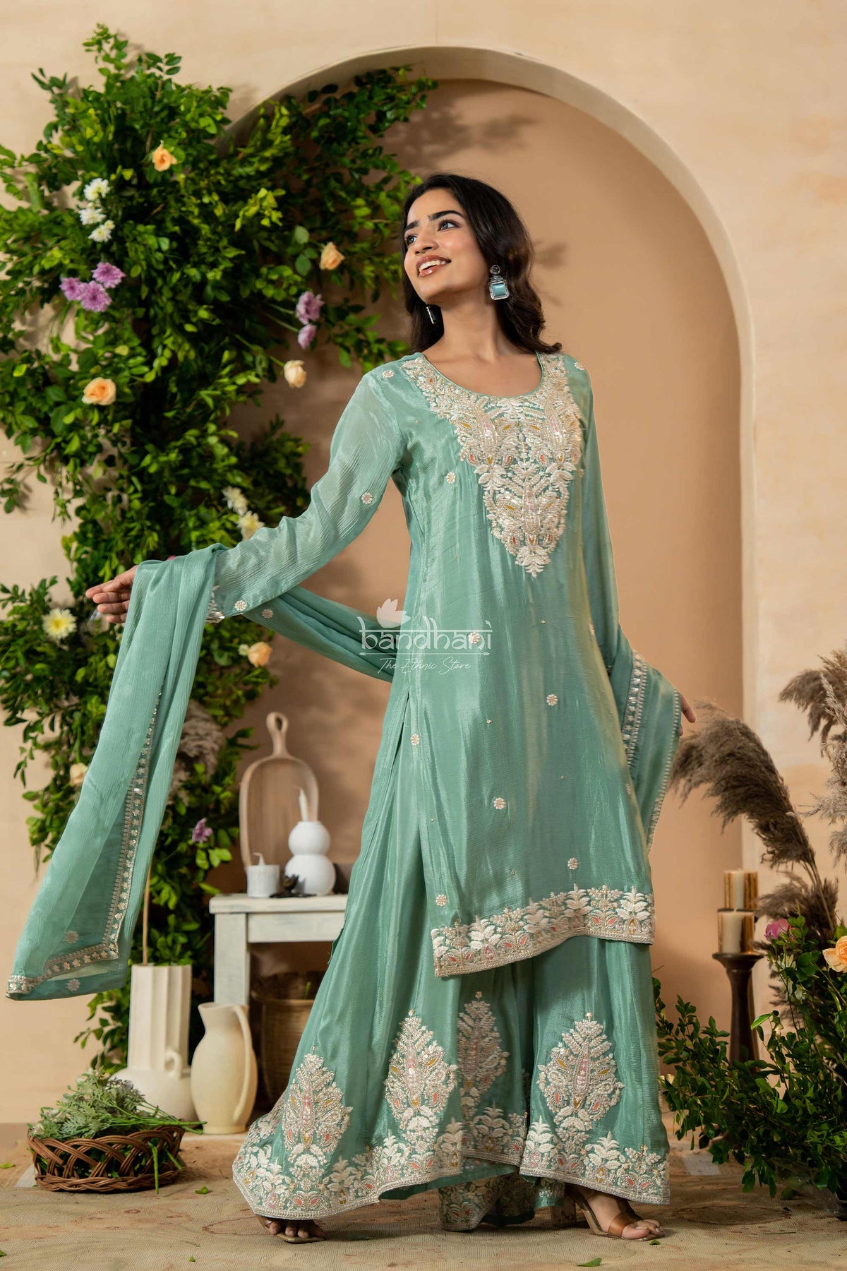 Woman in a light blue embroidered traditional outfit standing in a decorated outdoor setting.