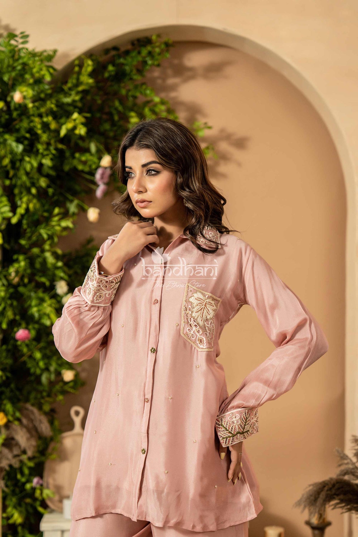 Woman wearing a pink embroidered outfit with a decorative background