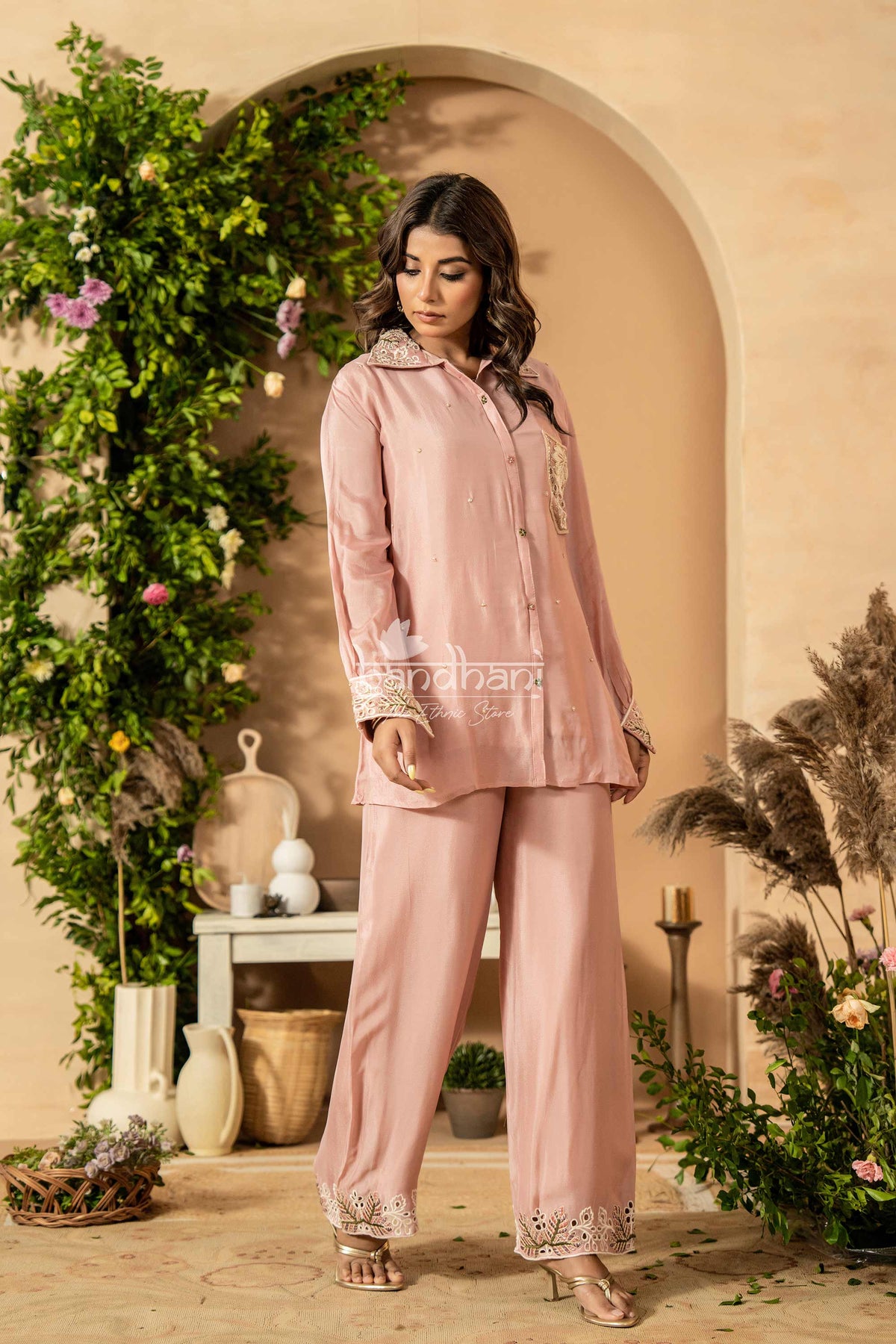 Woman in a pink outfit standing in a decorated indoor setting with plants and decor.