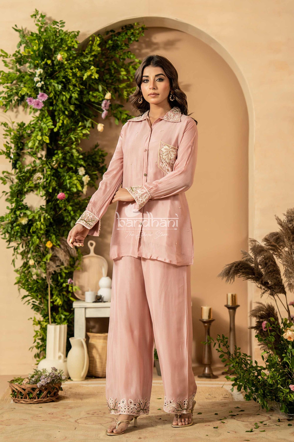 Woman in a pink outfit standing in a decorated room with plants and candles.