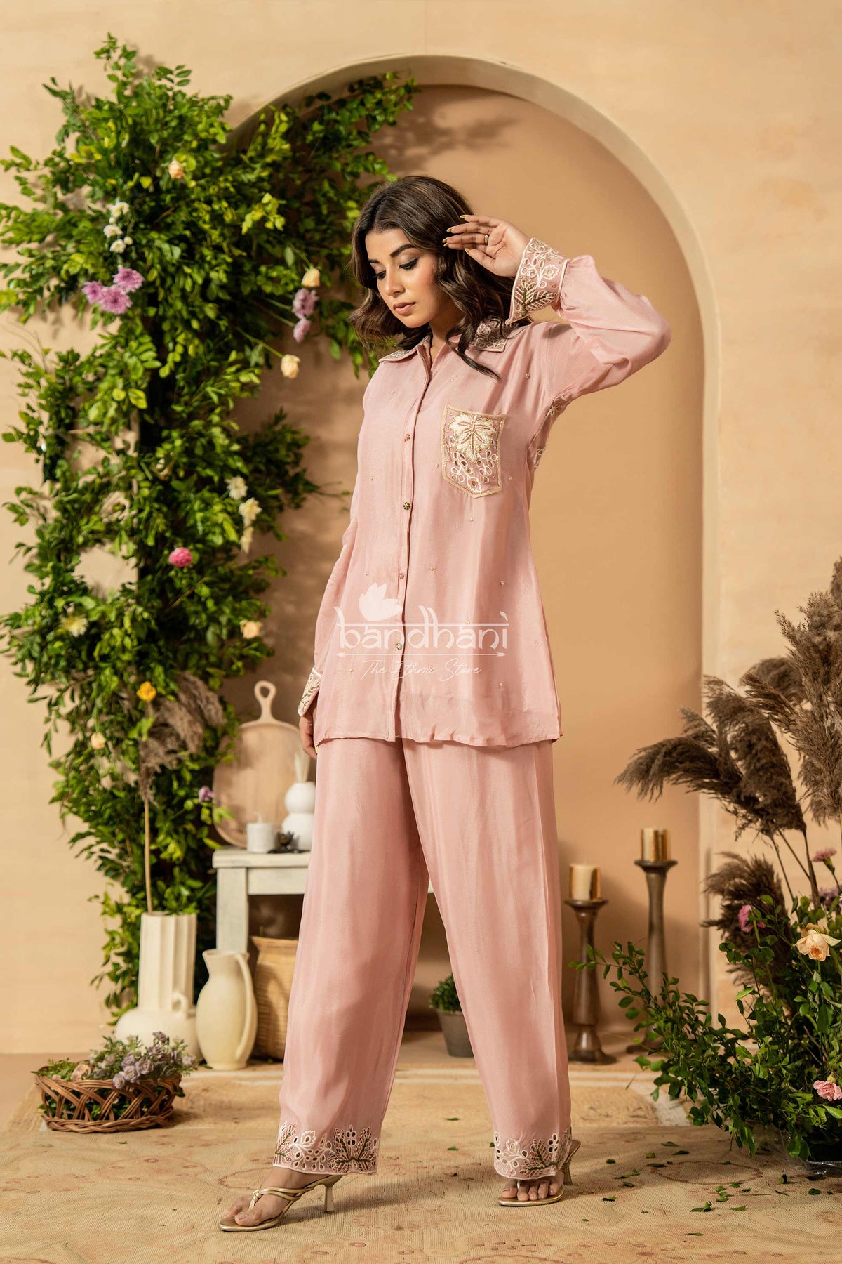 Woman wearing a pink pajama set with floral embroidery in a decorated room.