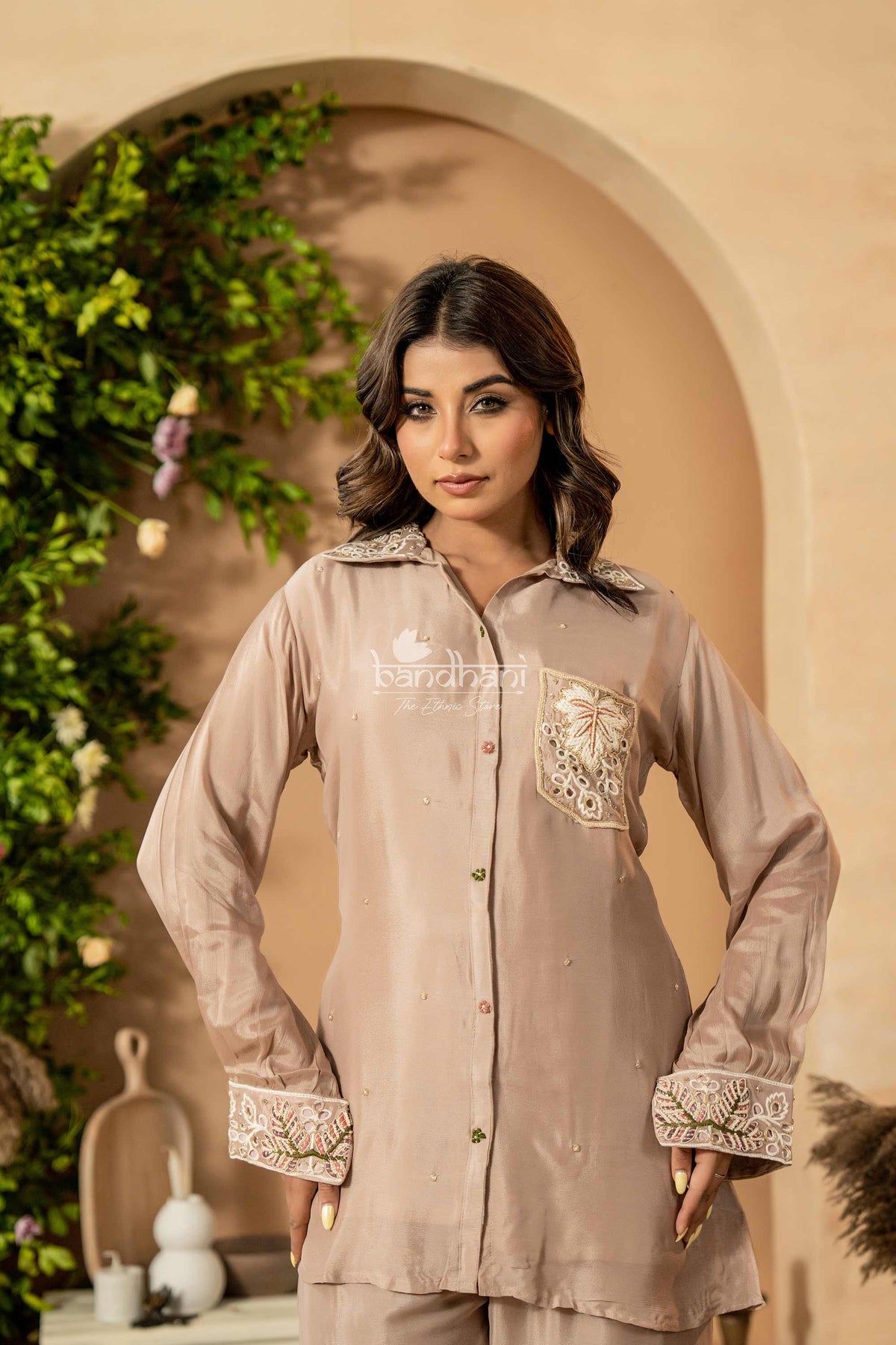 Woman wearing a beige embroidered outfit with a decorative background