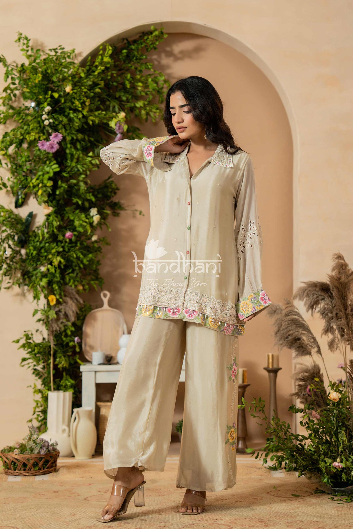 Woman in a beige outfit with floral embroidery standing in a decorated indoor setting.
