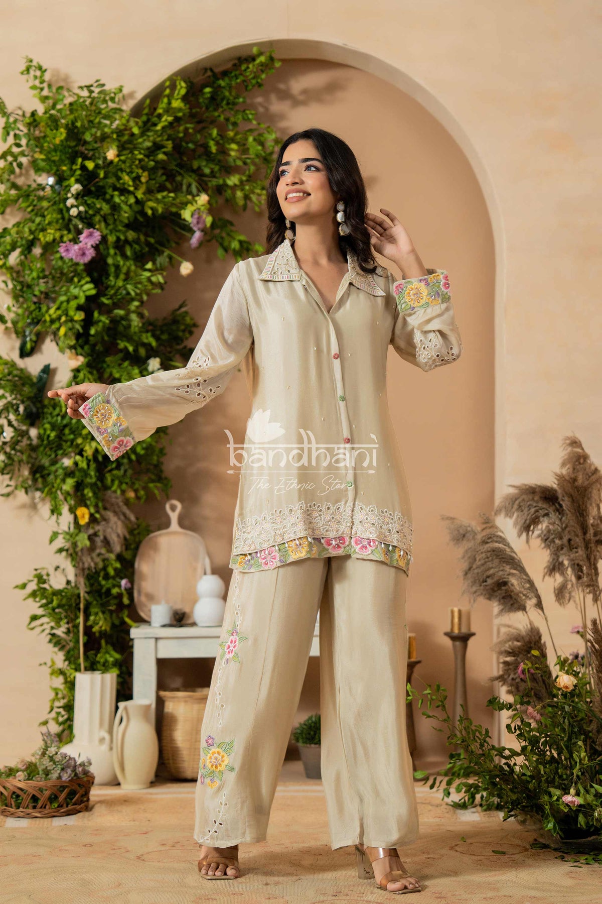 Woman in traditional outfit with floral embroidery standing in a decorated indoor setting.