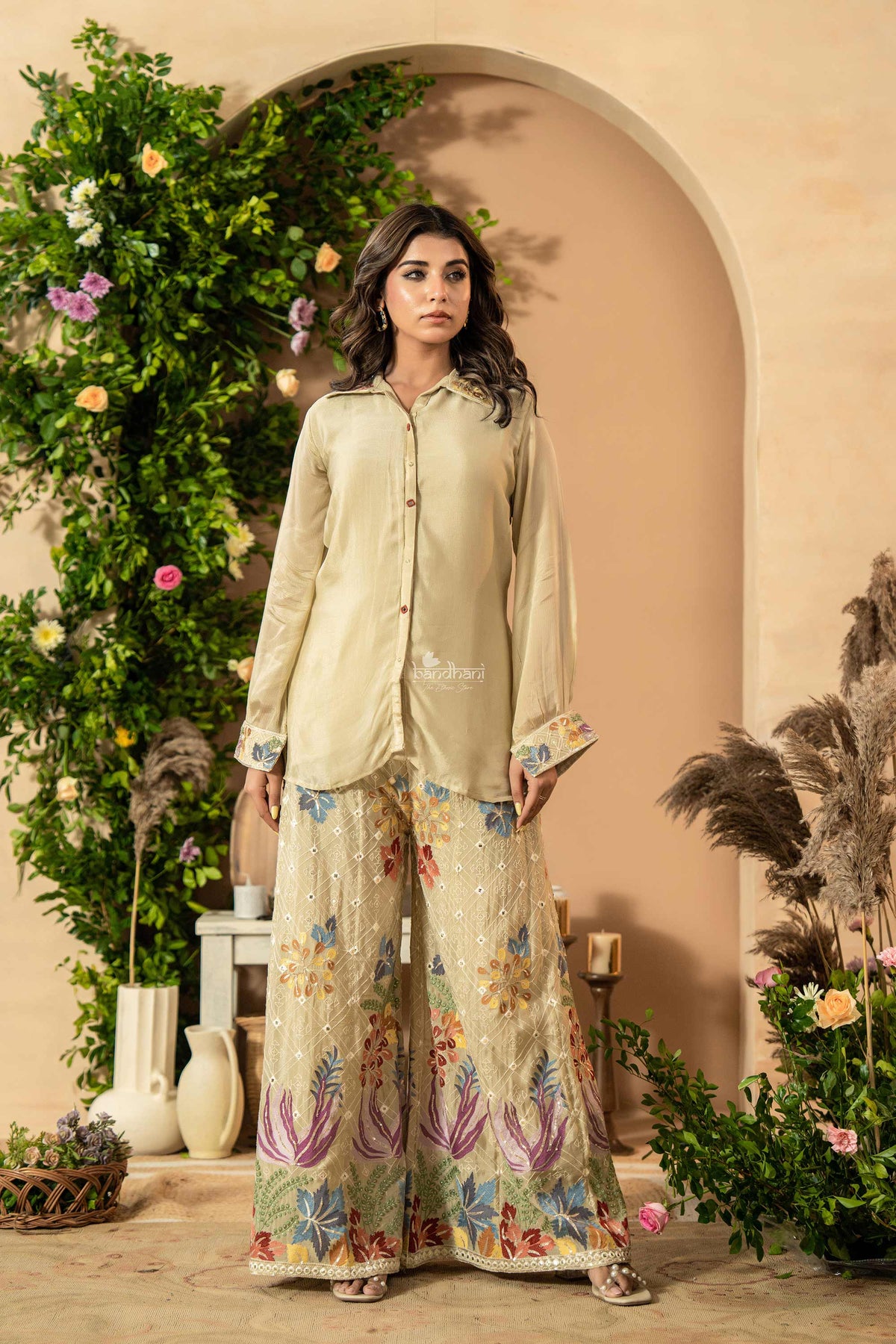 Woman in a light green outfit with floral patterns standing in a decorated indoor setting.