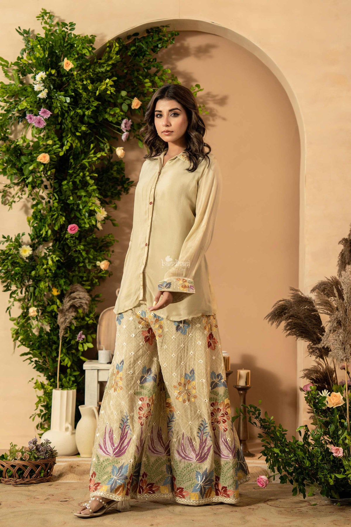 Woman in a floral outfit standing in a decorated room with plants and archway.