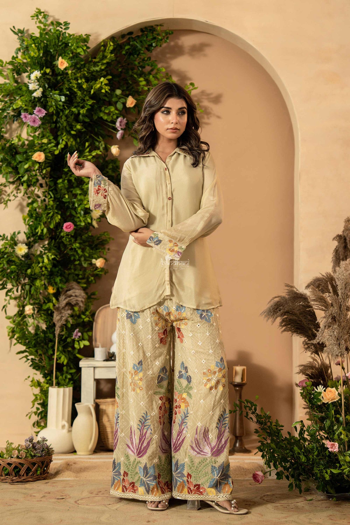 Woman in a floral outfit standing in a decorated room with plants and archway.