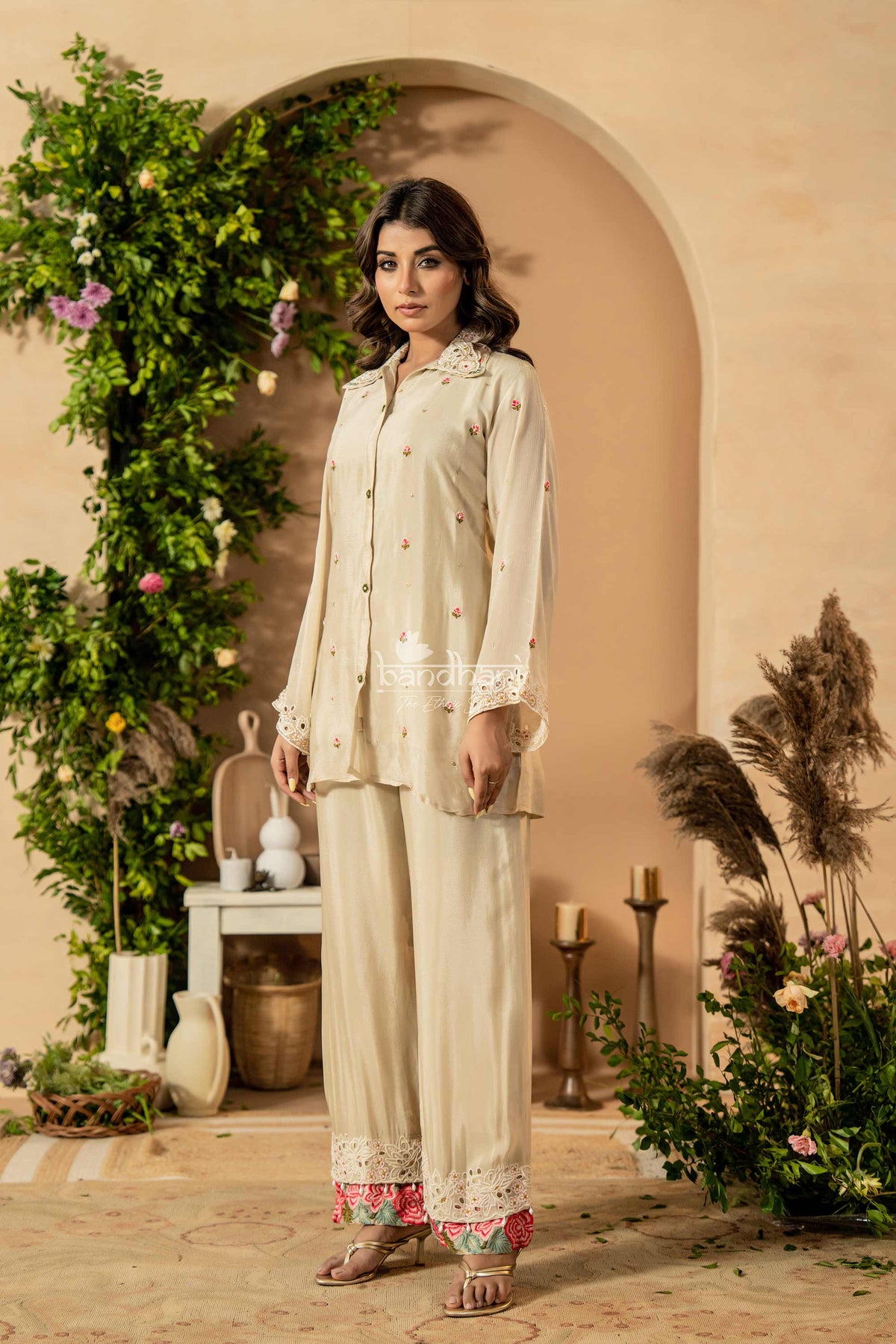Woman in a cream outfit standing in a decorated room with plants and candles.