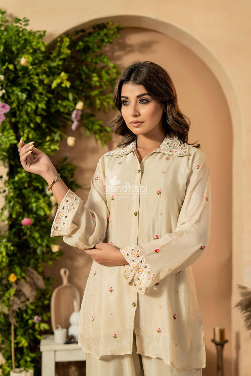 Woman wearing a cream-colored traditional outfit with floral patterns in an outdoor setting.