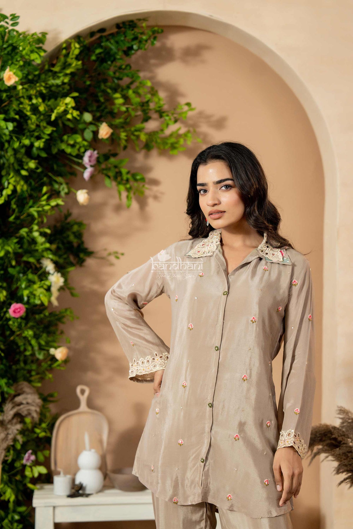 Woman wearing a beige outfit with floral details in a decorated room.