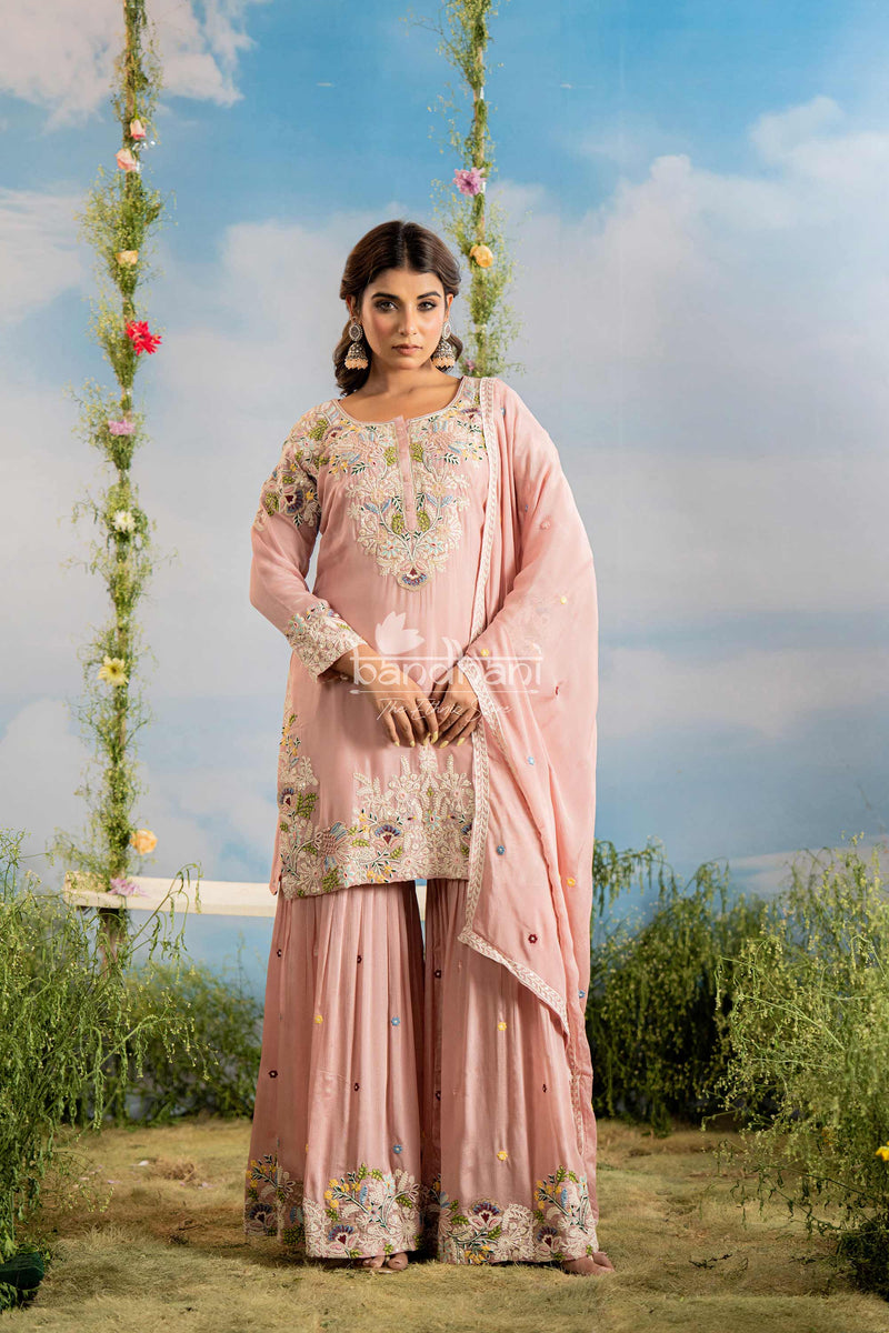 Woman in a pink traditional outfit with floral patterns standing outdoors against a blue sky.
